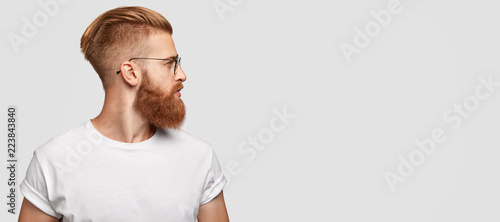 Photographie Sideways shot of brutal man with ginger thick beard, trendy hairstyle, looks tho