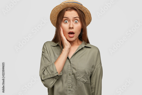 Portrait of amazed shocked terrible woman stares with eyes full of fear and disbelief, notices awful accident on road, wears fashionable summer hat, isolated over white background. Reaction concept