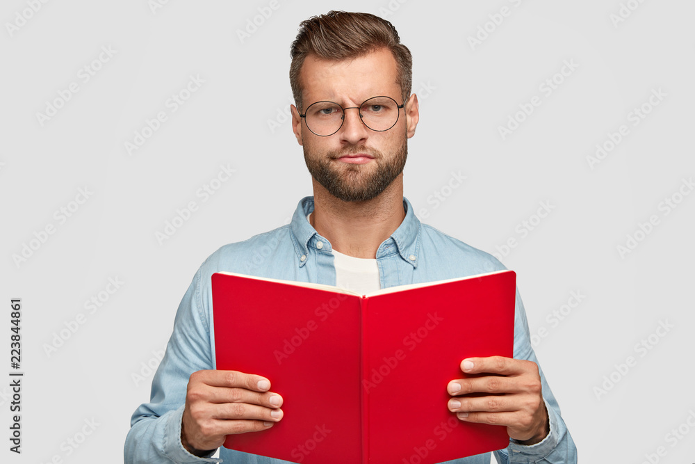 Displeased gloomy male teacher with bristle, uses book for preparing interesting material for lesson, doesnt like his job feels bored of reading wears round spectacles. Clever reader isolated on white Displeased gloomy male teacher with bristle, uses book for preparing interesting material for lesson, doesnt like his job feels bored of reading wears round spectacles. Clever reader isolated on white
