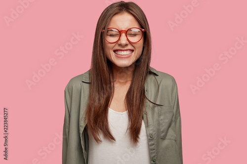 Obraz na płótnie Funny happy European woman with dark hair, broad smile, keeps eyes closed from p
