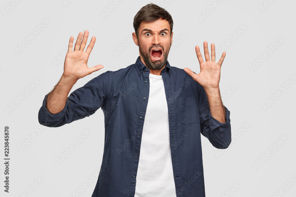 Annoyed unshaven man feels aversion, has disgusted expression, asks not bother him, keeps palms in front, looks with irritation, isolated over white background. Negative human emotions and feelings Annoyed unshaven man feels aversion, has disgusted expression, asks not bother him, keeps palms in front, looks with irritation, isolated over white background. Negative human emotions and feelings