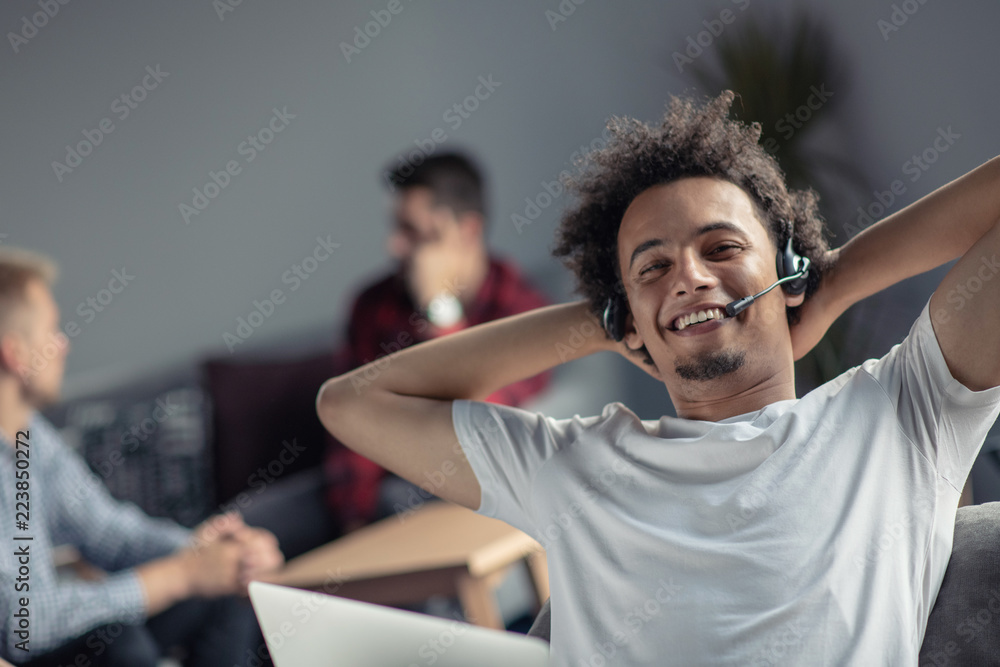 Satisfied relaxed african-american freelancer feeling happy at work sitting at office desk with headset.
