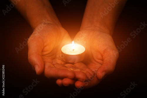 Hands holding and protecting glowing lit or burning candle candlelight on darkness. Black background. Concept for prayer, praying, hope, vigil, night watch
