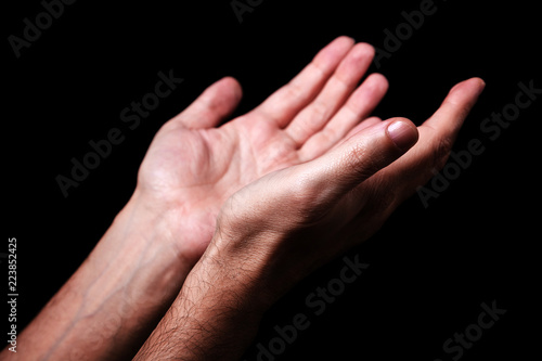 Male hands praying with palms up arms outstretched. Black background. Close up of man hand. Concept for prayer, faith, religion, religious, worship