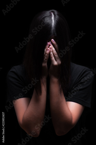 Emotional woman crying and covering the face with the hands hiding the tears, on a black or dark background. Concept for victim, depression, pain, grief, mourn, despair, sadness, fear.