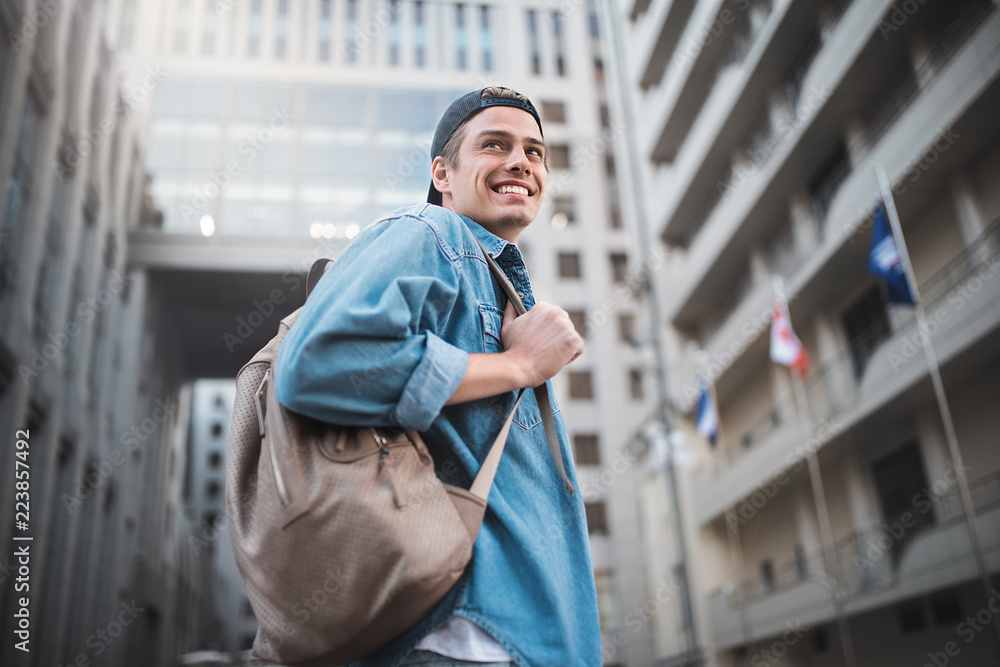 Naklejka premium Cheerful young man with backpack enjoying walk the city