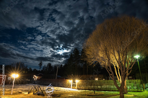 Swedish garden at night, full moon beside clouds, spring time, some winter snow left here