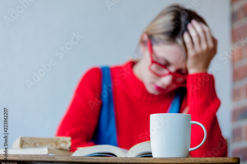 Young tired girl with cup of coffee and books at table.