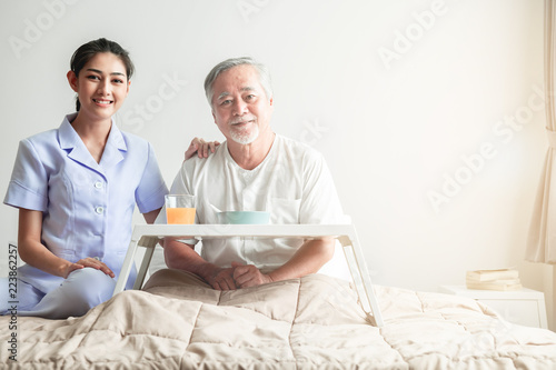 Young attractive nurse and senior man in bed portrait.