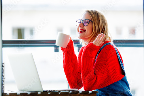 Young girl with cup and notebook computer sitting at table and working. Self business.