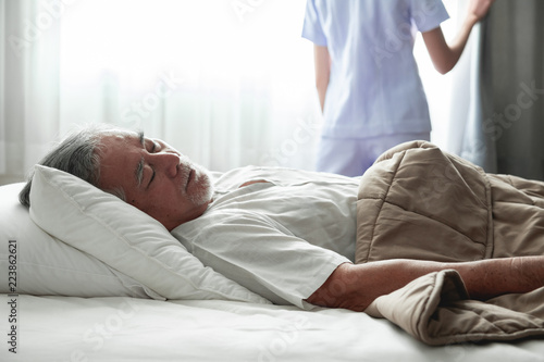 Senior man sleeping in bed and nurse open curtain.