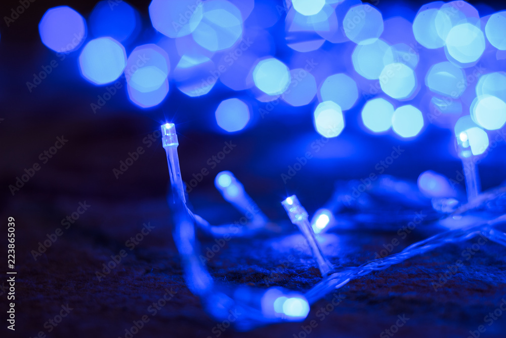 Christmas and New Year concept shot of blue garland lamps and illumination bokeh effect on dark abstract background Christmas and New Year concept shot of blue garland lamps and illumination bokeh effect on dark abstract background