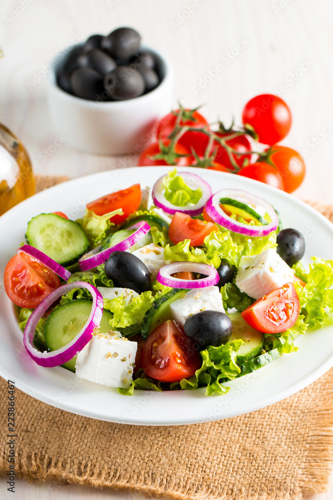 Fresh Greek salad made of cherry tomato, ruccola, arugula, feta, olives, cucumbers, onion and spices. Caesar salad in a white bowl on wooden background. Healthy organic diet food concept. Fresh Greek salad made of cherry tomato, ruccola, arugula, feta, olives, cucumbers, onion and spices. Caesar salad in a white bowl on wooden background. Healthy organic diet food concept.