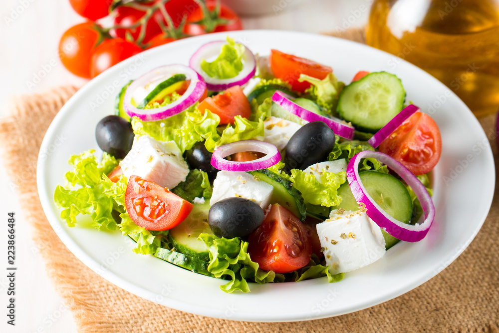 Fresh Greek salad made of cherry tomato, ruccola, arugula, feta, olives, cucumbers, onion and spices. Caesar salad in a white bowl on wooden background. Healthy organic diet food concept. Fresh Greek salad made of cherry tomato, ruccola, arugula, feta, olives, cucumbers, onion and spices. Caesar salad in a white bowl on wooden background. Healthy organic diet food concept.