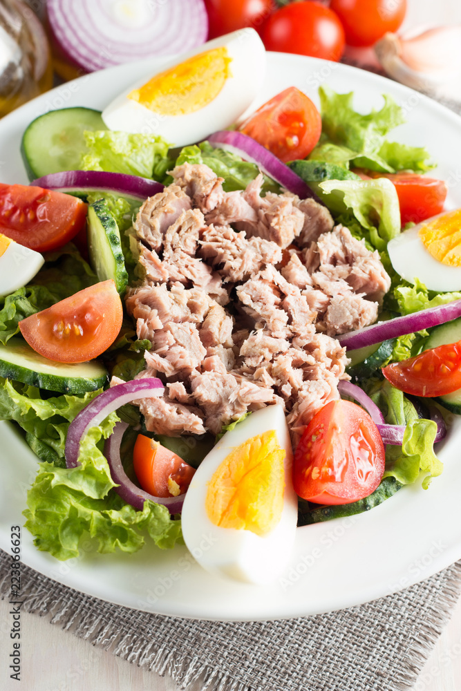 Fresh fish tuna salad made of tomato, ruccola, tuna, eggs, arugula, crackers and spices. Caesar salad in a white bowl on wooden background