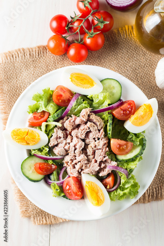 Fresh fish tuna salad made of tomato, ruccola, tuna, eggs, arugula, crackers and spices. Caesar salad in a white bowl on wooden background