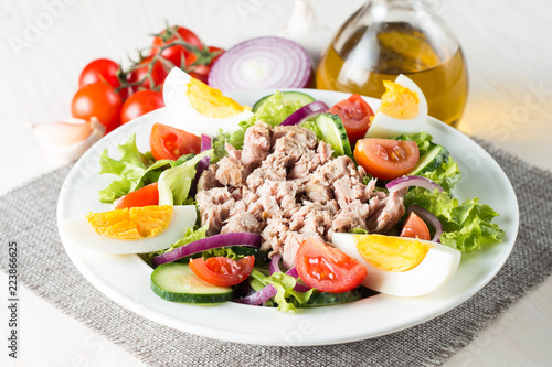 Fresh fish tuna salad made of tomato, ruccola, tuna, eggs, arugula, crackers and spices. Caesar salad in a white bowl on wooden background