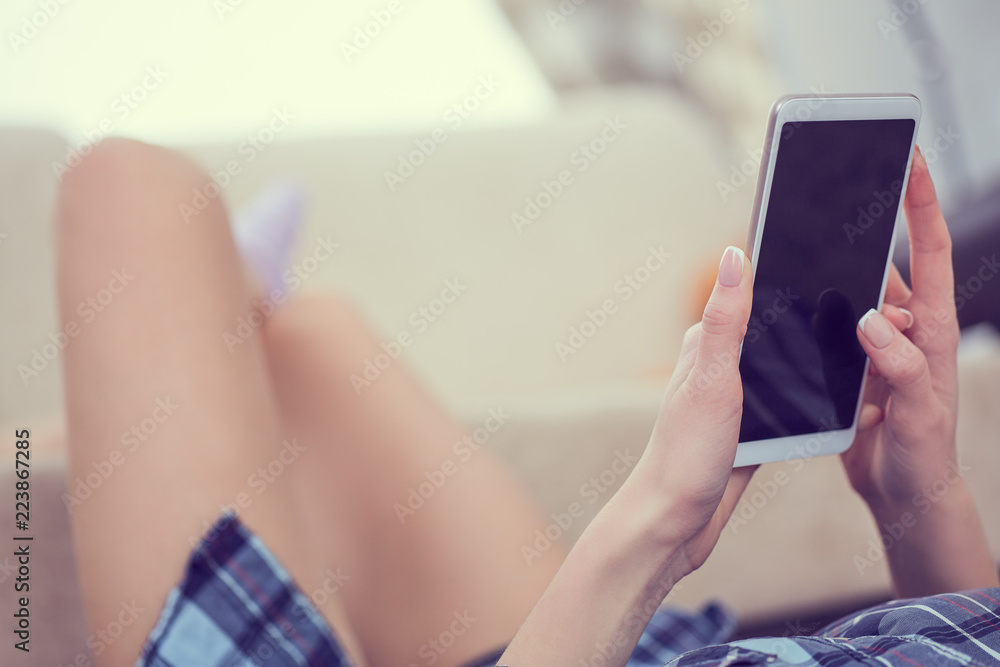 Back view of a woman hands using smart phone with blank screen close up. White phone with a black screen in the hands of a young girl lying on the floor with her feet on the couch Back view of a woman hands using smart phone with blank screen close up. White phone with a black screen in the hands of a young girl lying on the floor with her feet on the couch