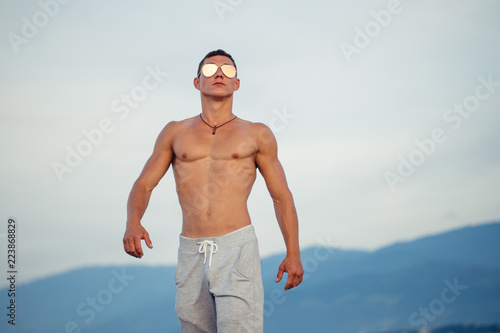 Masculine hard body man in sunglasses at beach with mountauns on background photo