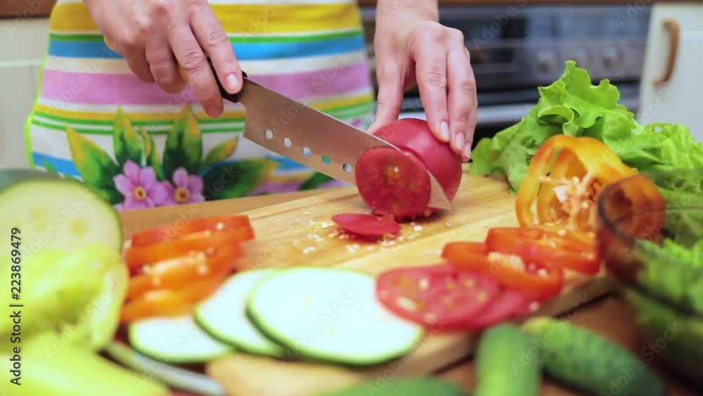 Women's hands Housewives cut with a knife fresh tomato on the cutting Board of the kitchen table Women's hands Housewives cut with a knife fresh tomato on the cutting Board of the kitchen table