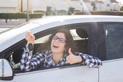 Young woman in car shows thumbs up and key photo