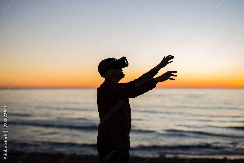 Fototapeta premium Young man using virtual reality glasses on over beautiful sky background