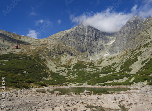 View on mountain Peak Lomnicky stit 2 634 m covered in clouds at Summer, in the High Tatras mountains of Slovakia with mountain lake Skalnate pleso and red cable car cabine, Vysoke Tatry