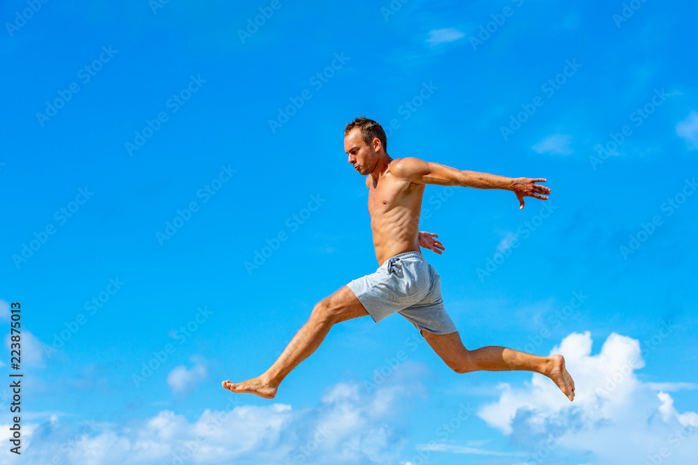 young man doing parkour jump on the blue sky background on sunny summer day