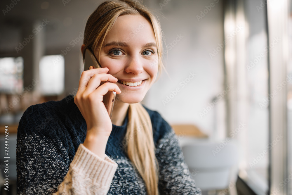 Portrait of attractive smiling woman with beautiful face sitting in modern cafe using mobile phone. Young successful female calling mobile. 