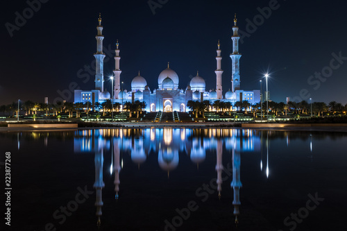 Grand Mosque in Abu Dhabi at night in the United Arab Emirates (UAE) in a Reflective Pond looking at the glowing Islamic iconic symbol. Ramadan call to prayer.