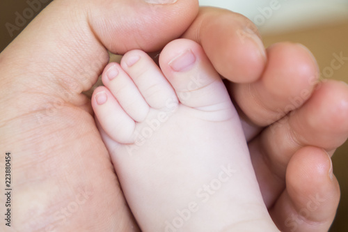 Father holds the leg of a newborn baby boy