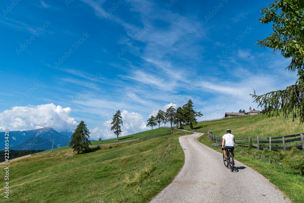 Mountainbiker fährt auf asphaltierter Straße über Wiese Mountainbiker fährt auf asphaltierter Straße über Wiese