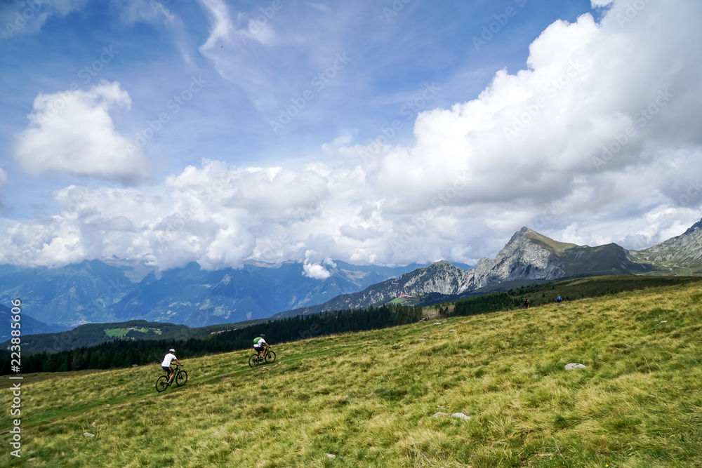 Fototapeta premium Zwei Mountainbiker über Wiese mit Panoramablick in die Berge