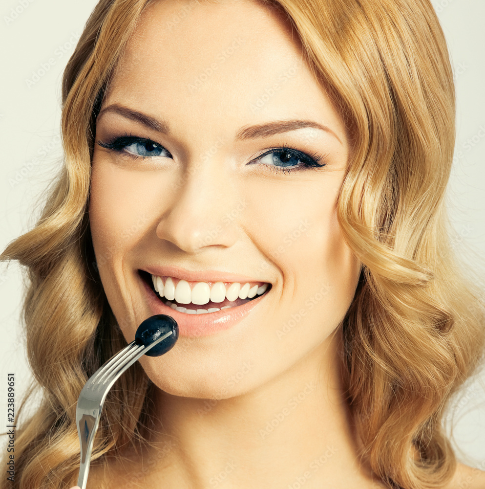 Young woman eating black olive, on grey Young woman eating black olive, on grey