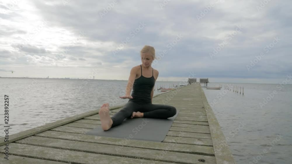 Beautiful young girl making yoga pose on the old wooden pier at the sea. Exercises calmness and harmony.
