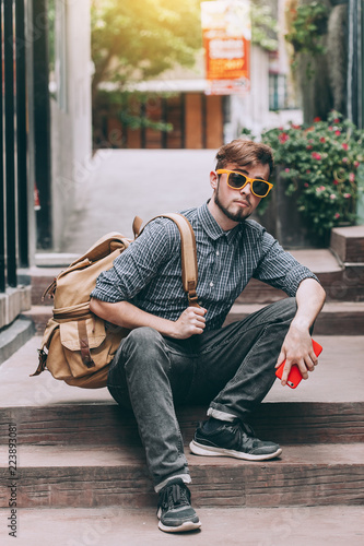 Traveler and tourist young man wearing backpack wearing yellow glasses using smartphone. travel backpack concept.