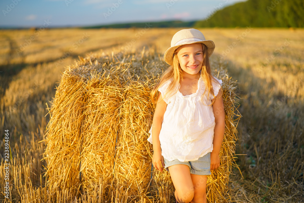 Little girl in a field with hay rolls at sunset