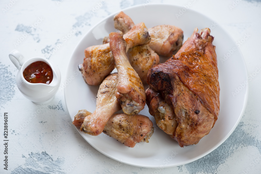 White plate with roasted turkey leg and chicken drumsticks, studio shot on a white concrete surface White plate with roasted turkey leg and chicken drumsticks, studio shot on a white concrete surface