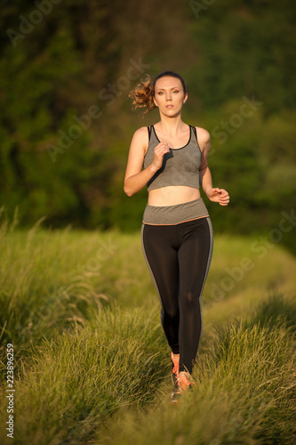 Beautiful young sporty woman workout in nature runs on a path on meadow