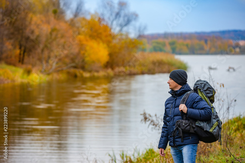 tourist holds a backpack with his hand and looks at the beauty of nature around him in the autumn near the river