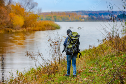 a tourist with a backpack on his shoulders walks along the river on a cold autumn day. A man dressed in warm clothes examines the area around