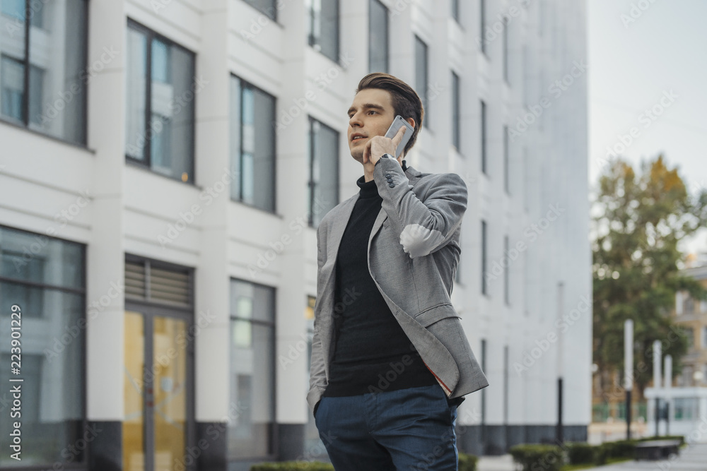 Distant plan of young businessman talking by mobile phone next to skyscraper. Distant plan of young businessman talking by mobile phone next to skyscraper.