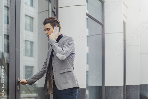 Distant plan of young business man talking by mobile phone and opening a door.