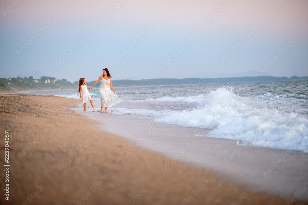 mother walking with her beloved daughter on the beach at sunset, holding hands and smiling