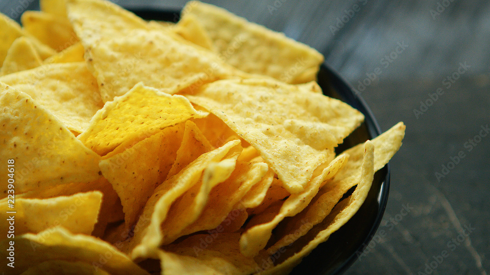 Closeup black plate full of crunchy golden nachos on wooden table Closeup black plate full of crunchy golden nachos on wooden table