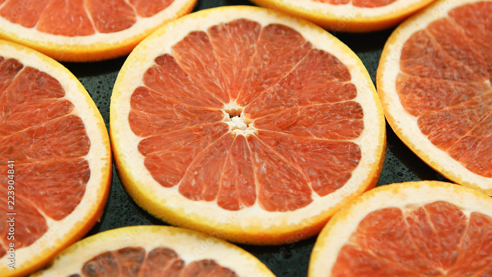 Closeup of composed round slices of cut grapefruit of bright ret color arranged together on glass surface Closeup of composed round slices of cut grapefruit of bright ret color arranged together on glass surface