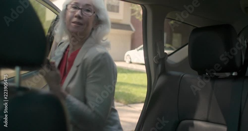 An older woman with a mobile phone checks the ride sharing app and verifies with the uber driver then moves contentedly to get into the back seat.