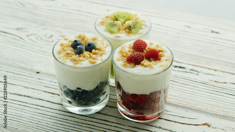Glass cups with berries in assortment and fresh white yogurt topped with granola and served on wooden table Glass cups with berries in assortment and fresh white yogurt topped with granola and served on wooden table
