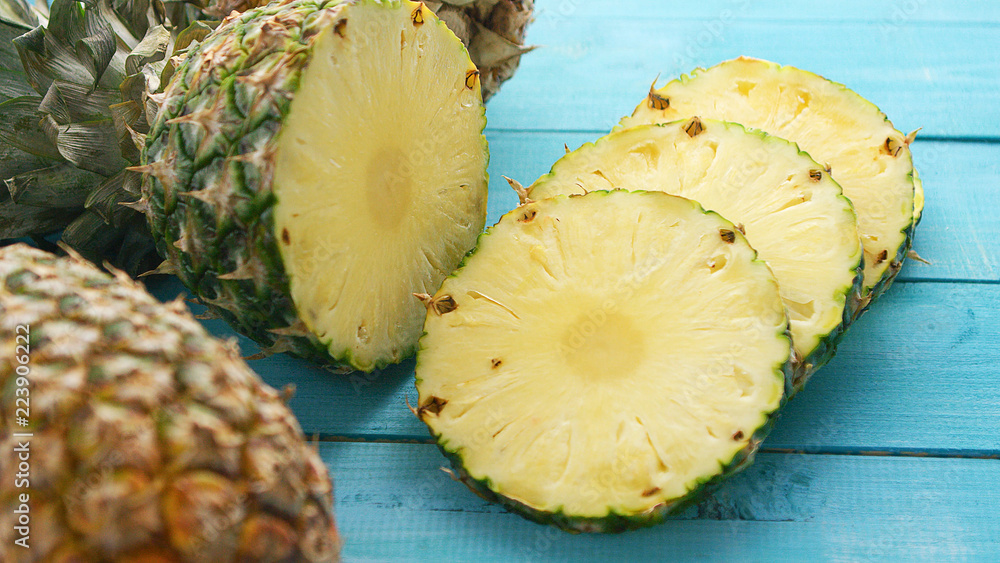 From above shot of composed unpeeled slices of freshly cut and served pineapple with juicy flesh on blue wooden surface From above shot of composed unpeeled slices of freshly cut and served pineapple with juicy flesh on blue wooden surface