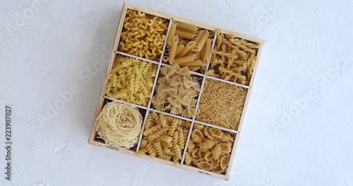 From above view of white box divided into sections with macaroni of different shape on white background